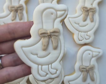 Op de afbeelding: Een verzameling eendvormige koekjes versierd met wit glazuur en een lichtbruine strik van glazuur bij de nek. Elk koekje heeft een gladde omtrek en een eenvoudig, strak ontwerp, gepresenteerd als een groep van individuele lekkernijen.