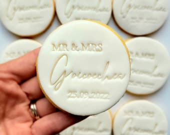 Op de afbeelding: Witte ronde koekjes met de tekst "MR & MRS Grococha 25.09.2022" en "MR & MRS Grococha" in gouden letters.