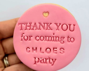 Op de afbeelding: Een ronde roze koekje met een gouden hartje en de tekst "Bedankt voor het komen naar Chloe's feestje" in roze.