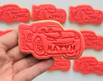 Op de afbeelding: Rode suikerkoekjes versierd met een cartoon afbeelding van een rode raceauto met nummer 3 aan de zijkant en de naam "MATYN" eronder.