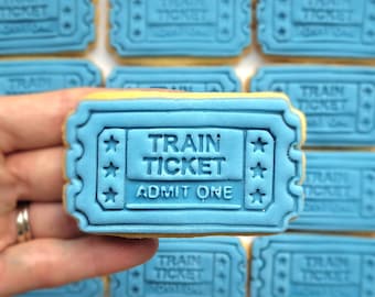 Op de afbeelding: Een blauwe en gele suikerkoek versierd met een treinkaartje-ontwerp. De koek heeft de tekst "Train Ticket" en "Admit One" in witte letters.