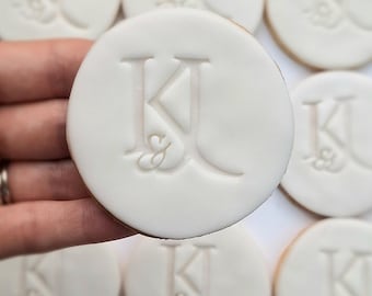 Op de afbeelding: Witte ronde koekjes met een monogram van de letters "K & J" in een decoratief schrift.