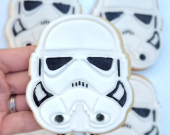 Op de afbeelding: Vier witte suikerkoekjes versierd met zwarte glazuur om te lijken op de iconische Star Wars Stormtrooper helm.