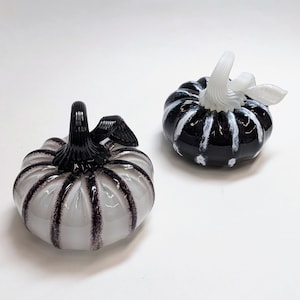 May include: Two glass pumpkins, one black with white stripes and one white with black stripes.