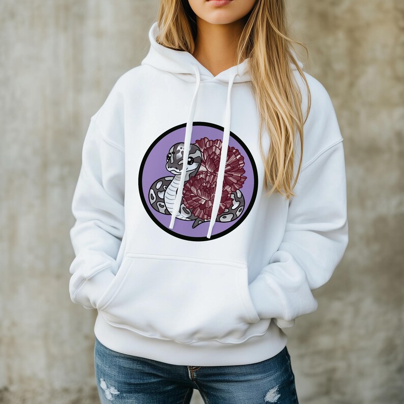 Może przedstawiać: Biała bluza z kapturem z przednią kieszenią i sznurkiem. Projekt to okrągła grafika z kresk&oacute;wkowym wężem i bordowym kwiatem na fioletowym tle. Wąż jest szary i biały z czarnymi plamami.