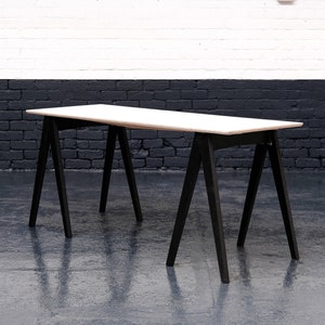 May include: A white rectangular table with a black trestle base. The table is made of wood and has a simple, modern design.