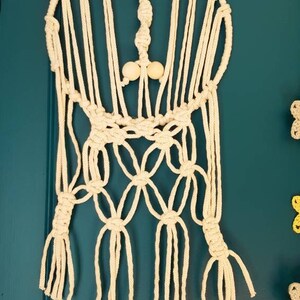 May include: A white macrame wall hanging with wooden beads. The hanging is made with a circular base and has a fringe at the bottom.