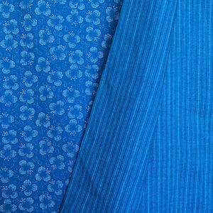 May include: Two pieces of blue fabric, one with a white floral pattern and the other with thin white stripes. The fabric is folded in half and the striped fabric is on top.