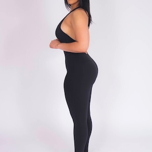 May include: A black one-piece jumpsuit with a halter neckline and a fitted silhouette. The jumpsuit has a smooth, stretchy fabric and is worn with white and black sneakers.