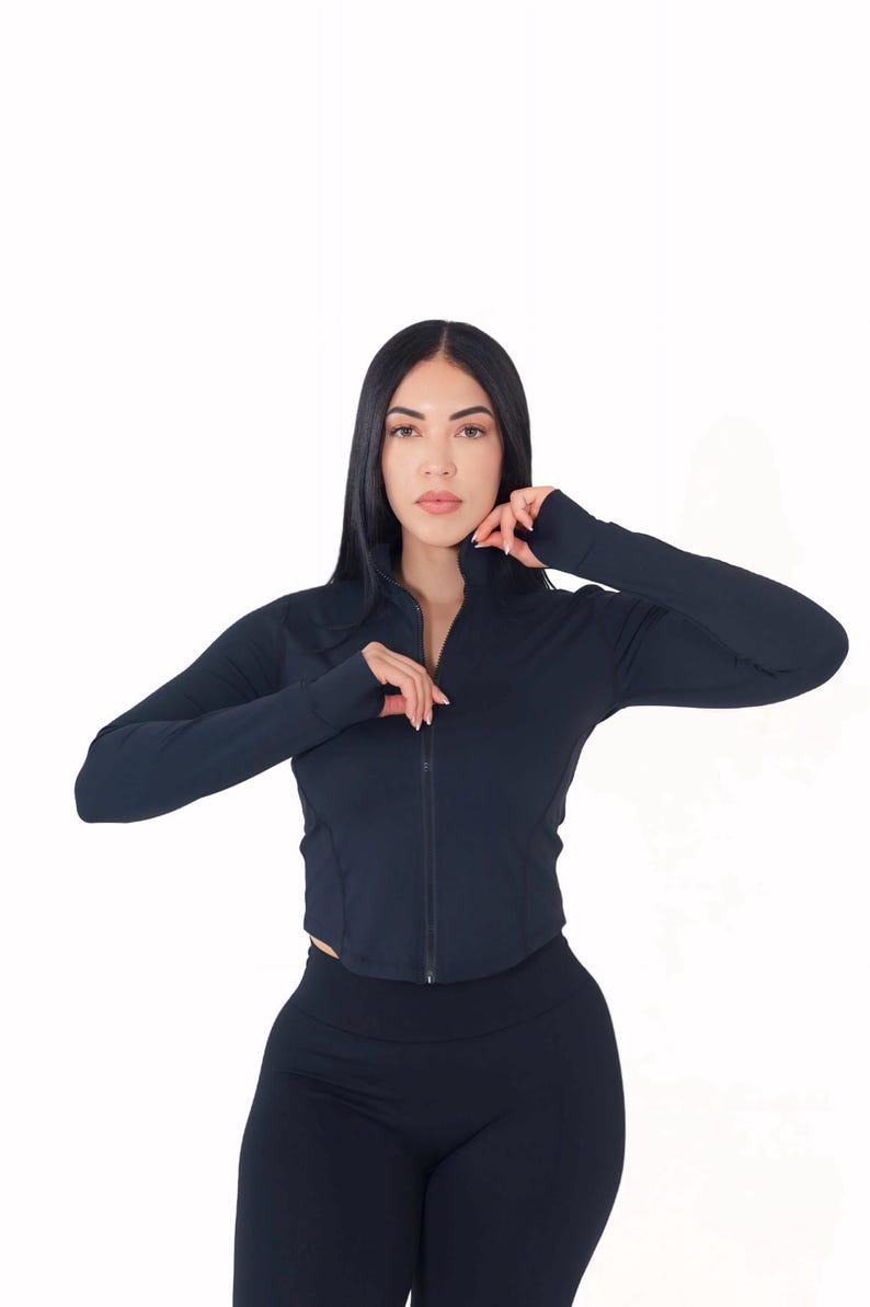 May include: A black long-sleeved zip-up jacket with a high neckline and thumbholes. The jacket is cropped and fitted.