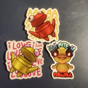 May include: Three cartoon stickers featuring stylized creatures. One is red with "AAAA" text, another is yellow with "I LOVE LOVE" text, and the last is yellow with "Will Bite if Provoked" text.