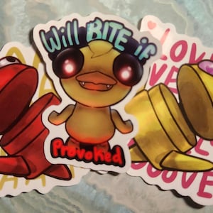 May include: A collection of stickers featuring cartoonish creatures and text. One sticker shows a yellow duck-like character with glowing red eyes and the words "Will Bite if Provoked." Other stickers have "Love" and "AA" text.
