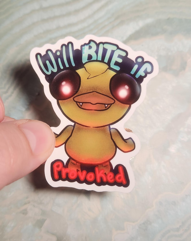 May include: A sticker featuring a cartoon duck with glowing red eyes and a menacing expression. The text "Will BITE if Provoked" is written above and below the duck in a playful font. The duck is yellow with orange accents.