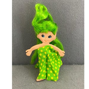 May include: A vintage doll with green hair and a green and yellow polka-dot outfit. The doll has blue eyes and outstretched arms. The doll's hair is styled in long, flowing waves. The doll is a whimsical, collectible item.