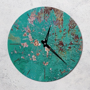 Può includere: Un orologio rotondo con un quadrante di colore verde acqua invecchiato e lancette nere. Il quadrante dell'orologio ha un aspetto arrugginito e invecchiato con accenti marroni.