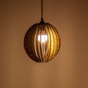 Könnte beinhalten: Eine runde Hängelampe aus Holz mit einem Lamellen-Schirm. Die Lampe ist eingeschaltet und beleuchtet den Raum.