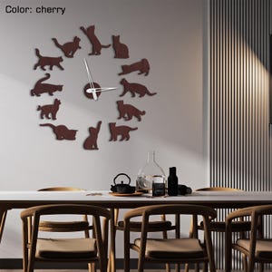 May include: Cherry-colored cat-shaped wall clock. The clock features a circular design with cat silhouettes marking the hours. The clock hands are white. The clock is mounted on a light gray wall above a dining table.