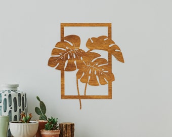 May include: A wooden wall decor featuring a cutout of two tropical leaves in a square frame. The leaves are brown and have a natural wood grain texture.