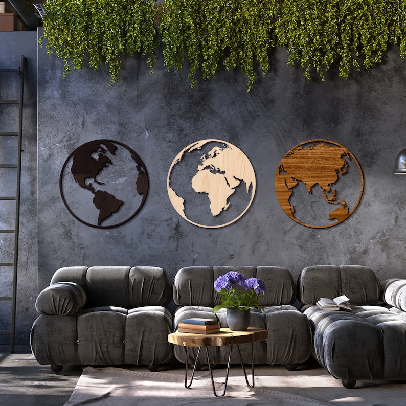 May include: Three wooden wall decor pieces shaped like the Earth, each with a different continent highlighted. The pieces are mounted on a gray wall above a gray couch.