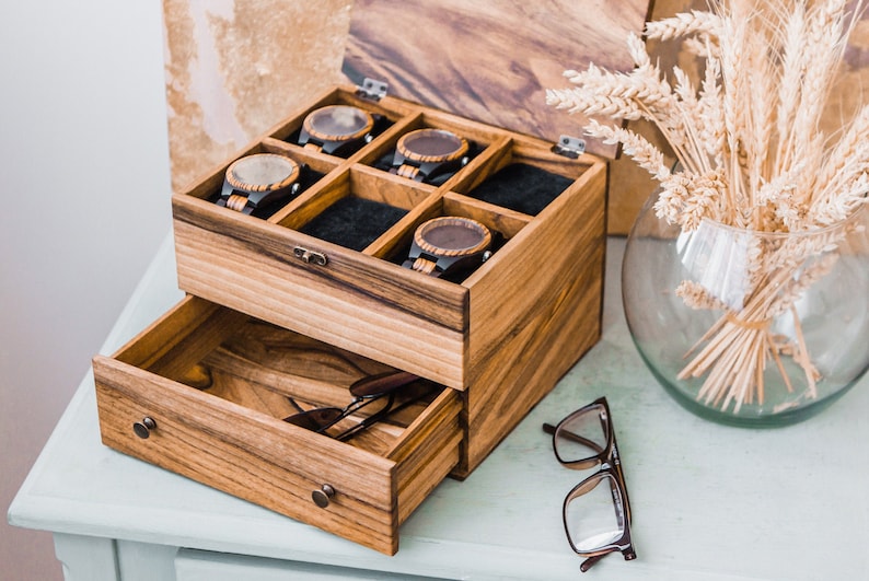 Pu&ograve; includere: Una scatola di legno con un cassetto, la parte superiore ha sei scomparti per riporre gli orologi. La scatola &egrave; aperta e il cassetto &egrave; tirato fuori, rivelando un paio di occhiali all'interno.