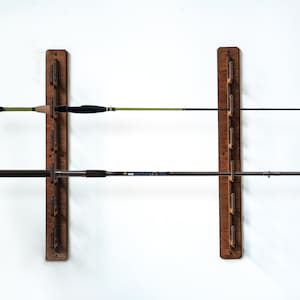 May include: A wooden wall-mounted fishing rod rack with two rows of rods. The rack is made of dark brown wood and has a simple design. The rods are black and green.