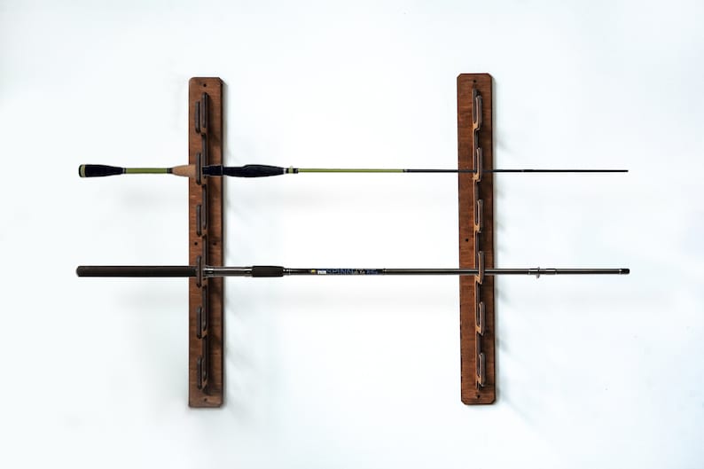 May include: A wooden wall-mounted fishing rod rack with two rows of rods. The rack is made of dark brown wood and has a simple design. The rods are black and green.