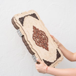 Könnte beinhalten: Ein dekorativer Wandbehang aus Holz mit aufwendigen Schnitzereien in Braun und Beige. Das Design zeigt ein zentrales florales Motiv mit einem geometrischen Muster.