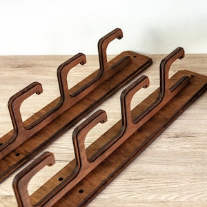May include: Two wooden wall-mounted coat racks with three hooks each. The racks are made of dark brown wood and have a natural wood grain finish.