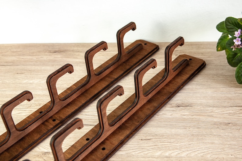 May include: Two wooden wall-mounted coat racks with three hooks each. The racks are made of dark brown wood and have a natural wood grain finish.