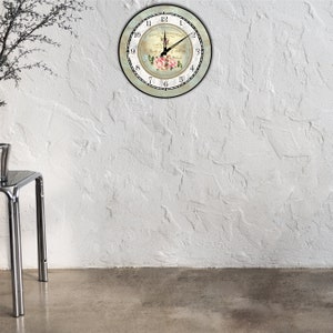 Pu&ograve; includere: Un orologio da parete rotondo con cornice nera e bordo verde chiaro. Il quadrante presenta un motivo floreale con rose rosa e il testo "BELLE JARDINIERE". Le lancette dell'orologio sono nere.