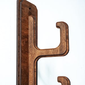 May include: A wooden wall mount with two hooks for hanging items. The mount is made of dark brown wood and has a smooth finish.