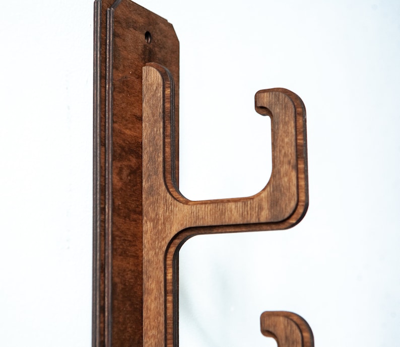 May include: A wooden wall mount with two hooks for hanging items. The mount is made of dark brown wood and has a smooth finish.