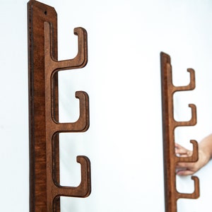 May include: Two wooden wall mounted coat racks with four hooks each. The racks are made of dark brown wood and have a natural wood grain finish.