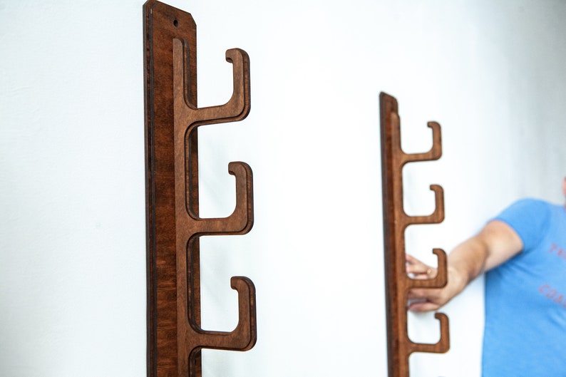 May include: Two wooden wall mounted coat racks with four hooks each. The racks are made of dark brown wood and have a natural wood grain finish.