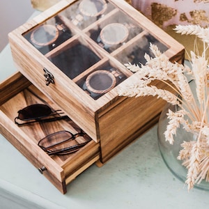 Pu&ograve; includere: Una scatola di legno con un coperchio di vetro e un cassetto. La scatola ha scomparti per riporre gli orologi e il cassetto &egrave; per riporre gli occhiali da sole. La scatola &egrave; realizzata in legno marrone chiaro e ha una finitura naturale.
