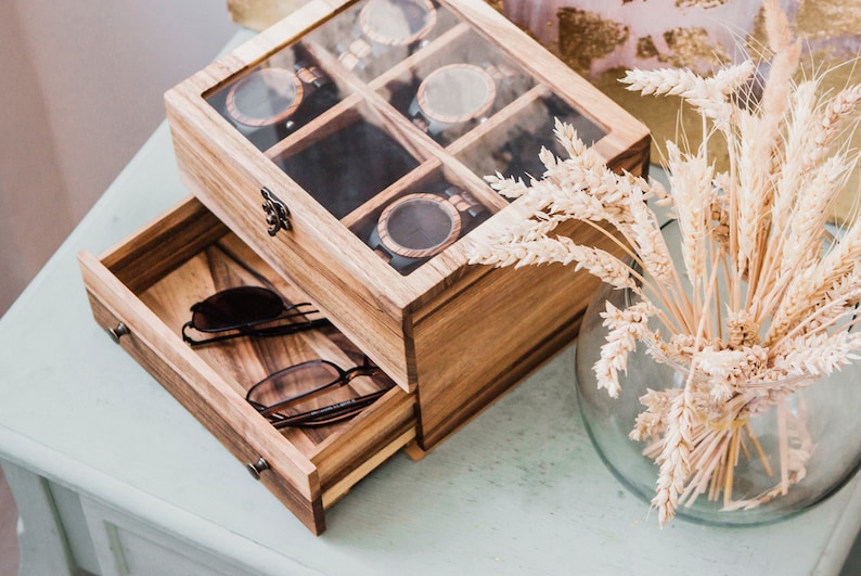 Pu&ograve; includere: Una scatola di legno con un coperchio di vetro e un cassetto. La scatola ha scomparti per riporre gli orologi e il cassetto &egrave; per riporre gli occhiali da sole. La scatola &egrave; realizzata in legno marrone chiaro e ha una finitura naturale.