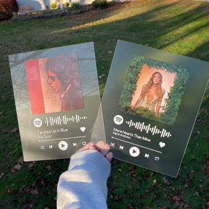 May include: Two transparent acrylic plaques, each with album art and a Spotify-style interface. One shows "Tangled Up In Blue" by Bob Dylan, the other "More Hearts Than Mine" by Ingrid Andress. They are held against a green grass background.