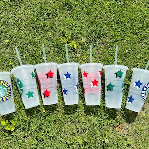 May include: Seven clear plastic cups with straws, each decorated with a different university logo and stars in red, blue, and green. The logos include Quinnipiac University, Villanova University, and other university names.