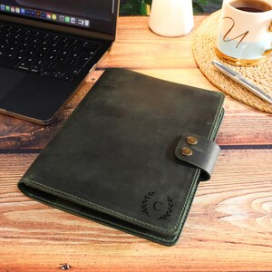 Può includere: Un'agenda in pelle verde scuro con chiusura a fibbia in ottone e un monogramma con l'iniziale "C" in un design a corona di alloro.