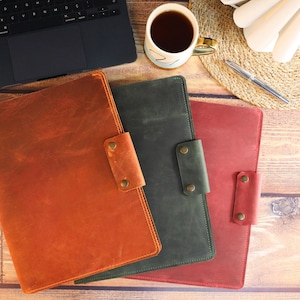 May include: Three leather laptop sleeves in different colors: brown, green, and red. The sleeves have a flap closure with a snap button.