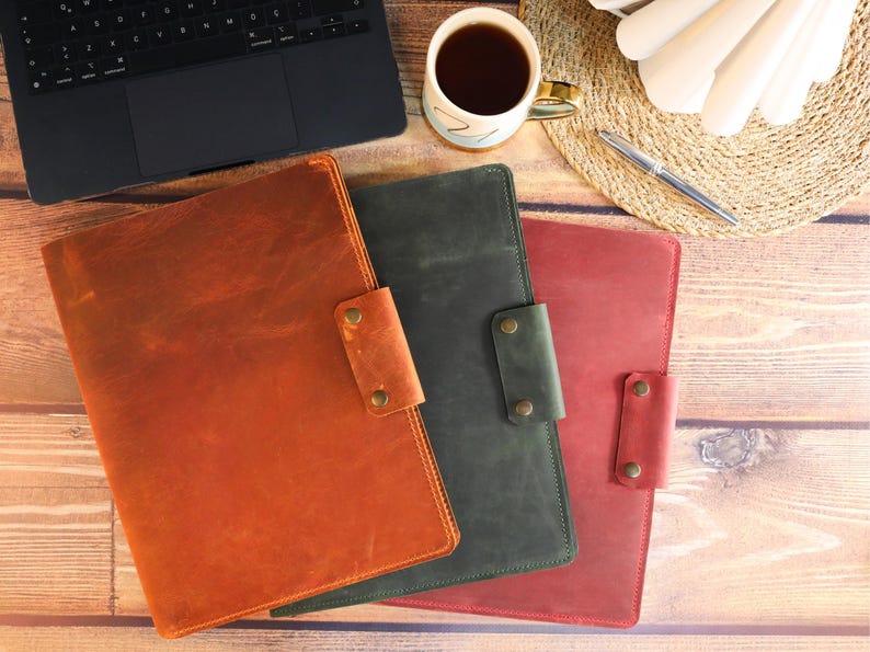 May include: Three leather laptop sleeves in different colors: brown, green, and red. The sleeves have a flap closure with a snap button.