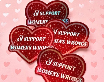 Op de afbeelding: Drie rode hartvormige stickers met een glinsterende afwerking. Elke sticker heeft de tekst "I Support" en dan "Women's Wrongs" of "Men's Wrongs".