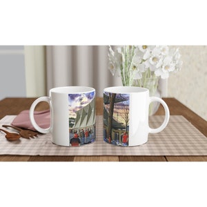 Puede incluir: Dos tazas de cerámica blanca con una ilustración colorida de un estadio y personas. La taza de la izquierda tiene un asa en el lado izquierdo y la taza de la derecha tiene un asa en el lado derecho.