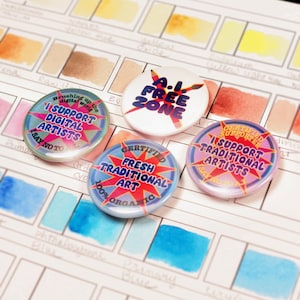 May include: Four circular pin badges are displayed on a watercolour swatch sheet. The badges feature text such as "A.I. FREE ZONE" and "I SUPPORT DIGITAL ARTISTS." The background is a grid of watercolour swatches in a variety of colours, including blues and yellows.