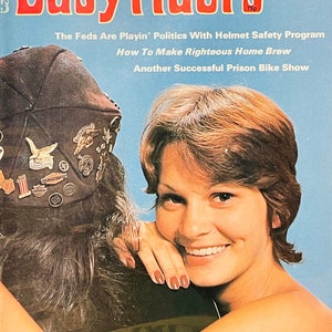以下が含まれることがあります： Easyridersというオートバイ雑誌の表紙で、長い茶色の髪をした女性が笑顔で、ひげを生やした男性が革のジャケットとオートバイのヘルメットを着用しています。表紙のテキストには、「Entertainment for Adult Bikers」、「October, 1977」、「$1.25」、「The Feds Are Playin' Politics With Helmet Safety Program」、「How To Make Righteous Home Brew」、「Another Successful Prison Bike Show」、「Women's Greatest Worry -And Lotsa Other Disgustin' Stuff!」とあります。