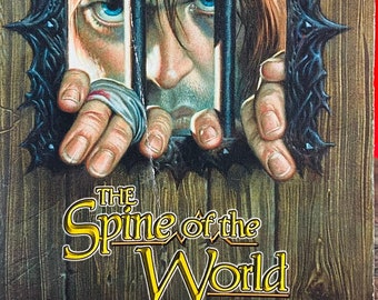 May include: A paperback fantasy novel titled "The Spine of the World" by R.A. Salvatore. The cover features a man with blue eyes behind bars, with a sneak preview of his new hardcover "Servant of the Shard".