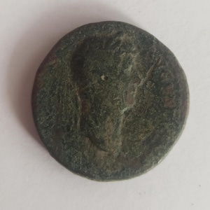 Puede incluir: Una moneda de bronce con un retrato de una persona en un lado. La moneda está desgastada y tiene una pátina verde.