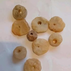 May include: A collection of eight off-white, round, stone beads with a hole in the center. The beads are various sizes and shapes.
