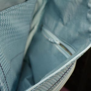K&ouml;nnte beinhalten: Nahaufnahme des Inneren einer hellblauen Jeans-Tasche. Die Tasche hat eine Rei&szlig;verschlusstasche und ein hellblaues Futter. Der Rei&szlig;verschluss ist wei&szlig;. Der Innenstoff hat ein dezentes Fischgr&auml;tenmuster.