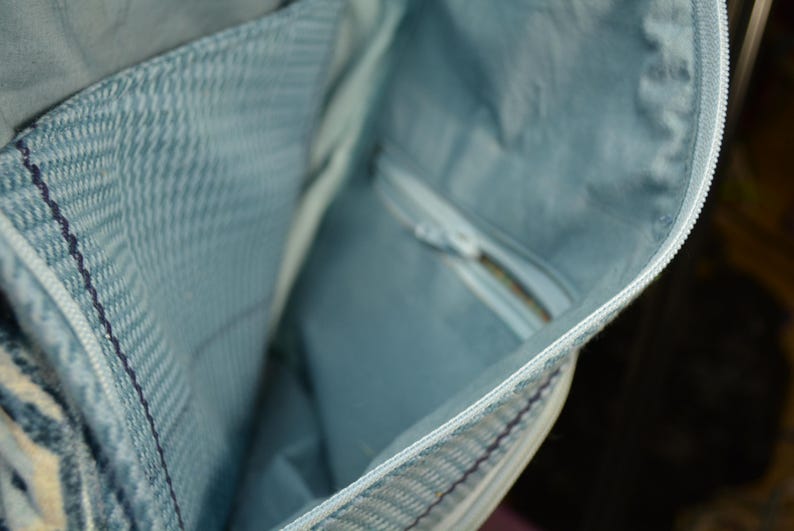 K&ouml;nnte beinhalten: Nahaufnahme des Inneren einer hellblauen Jeans-Tasche. Die Tasche hat eine Rei&szlig;verschlusstasche und ein hellblaues Futter. Der Rei&szlig;verschluss ist wei&szlig;. Der Innenstoff hat ein dezentes Fischgr&auml;tenmuster.